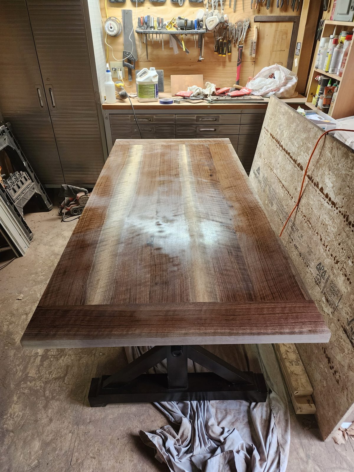 Walnut dining table top on a dark trestle base in the workshop