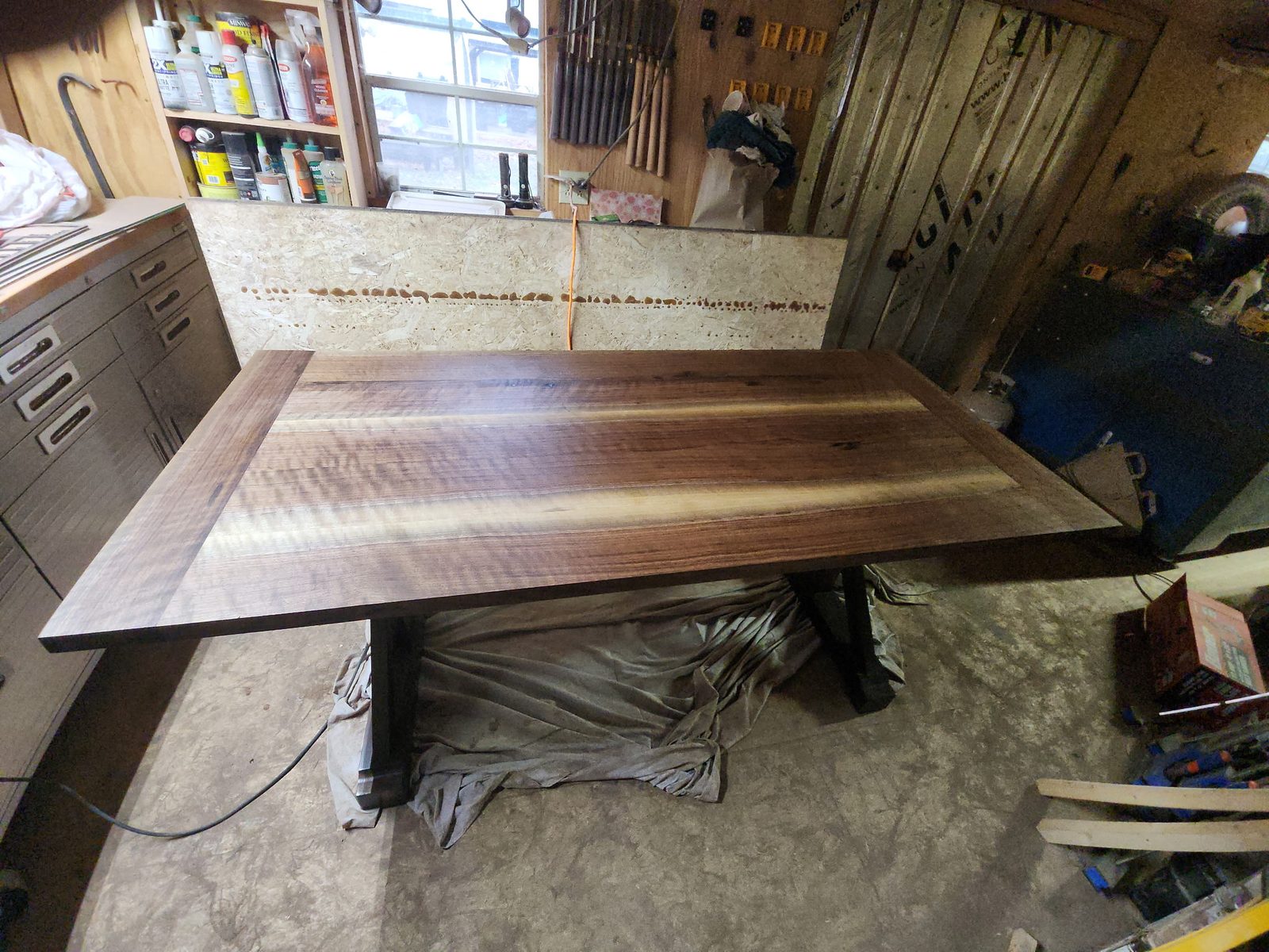 Walnut tabletop laid across its base in the workshop